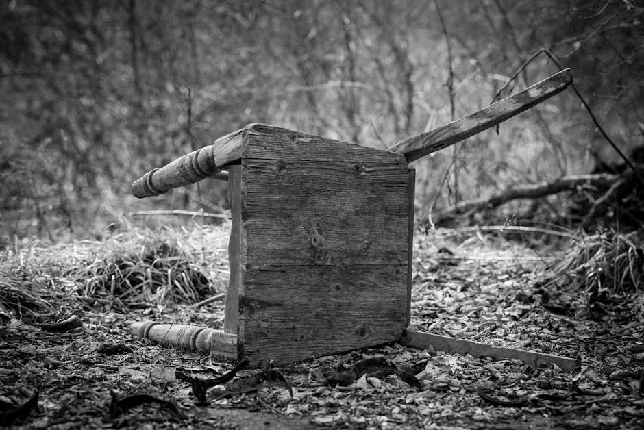 A discarded broken wooden chair lies on the ground amidst dry leaves in a forested area.
