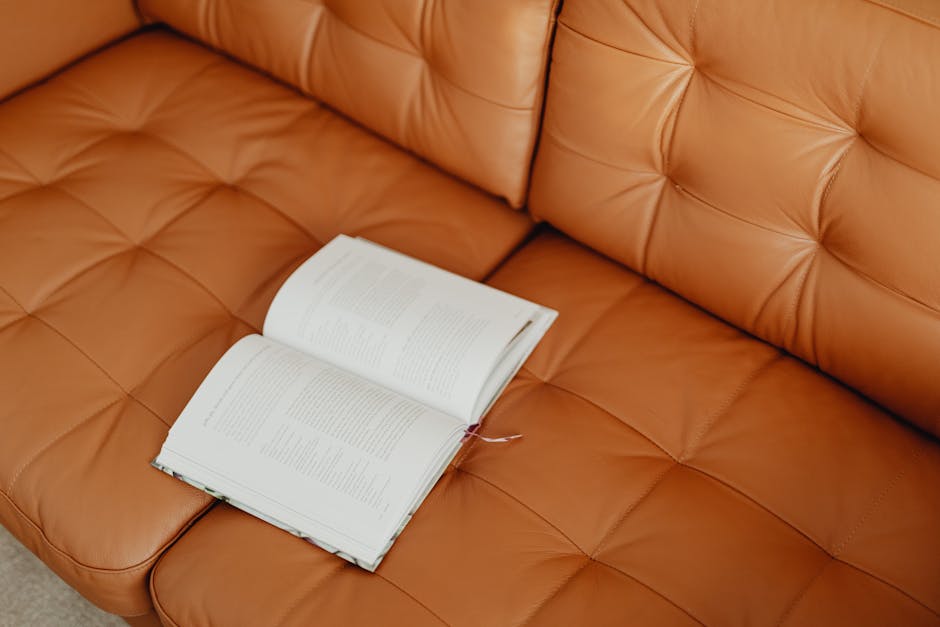 An open book lies on a stylish brown leather sofa, symbolizing leisure and relaxation.