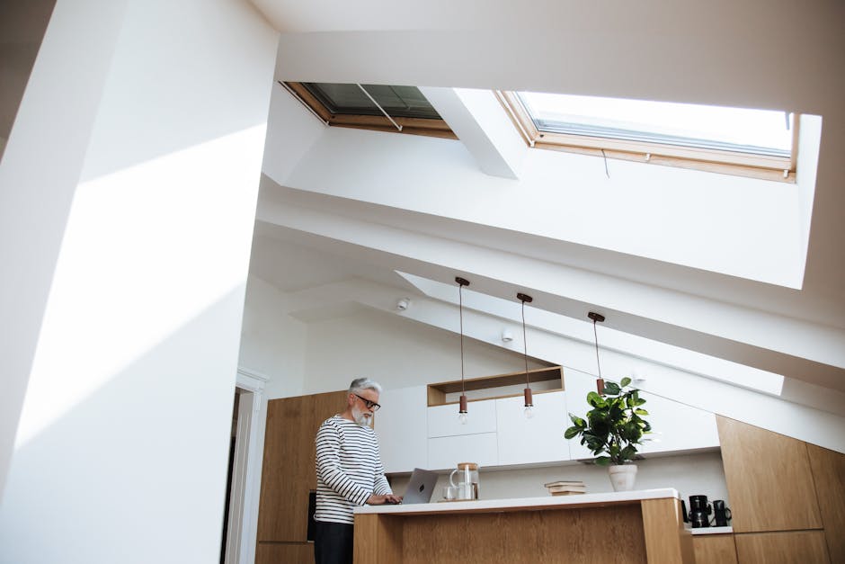 Gray-haired man at home office using laptop in bright kitchen space.