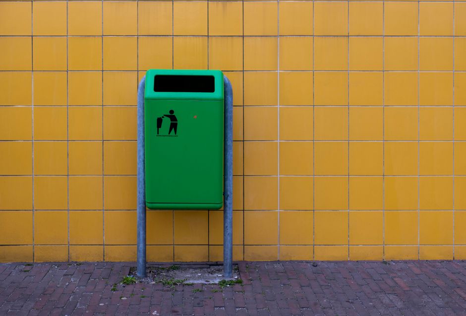 A green trash bin standing against a vibrant yellow tiled wall, conveying urban cleanliness.