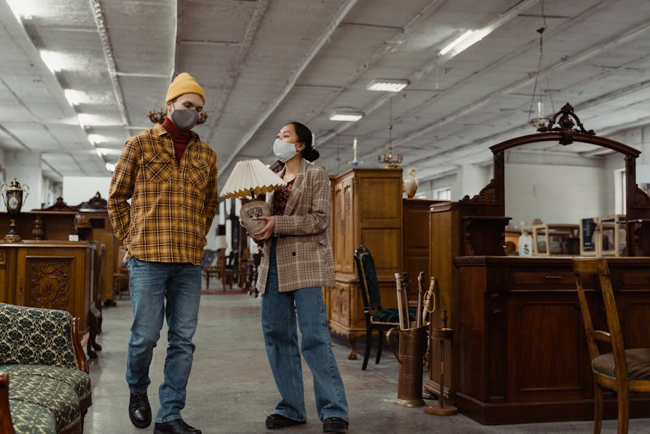 A man and woman in face masks shop for vintage furniture in a spacious antique store.