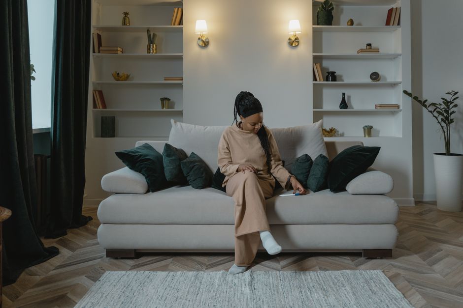 A pregnant woman sits thoughtfully on a couch in a cozy living room setting.