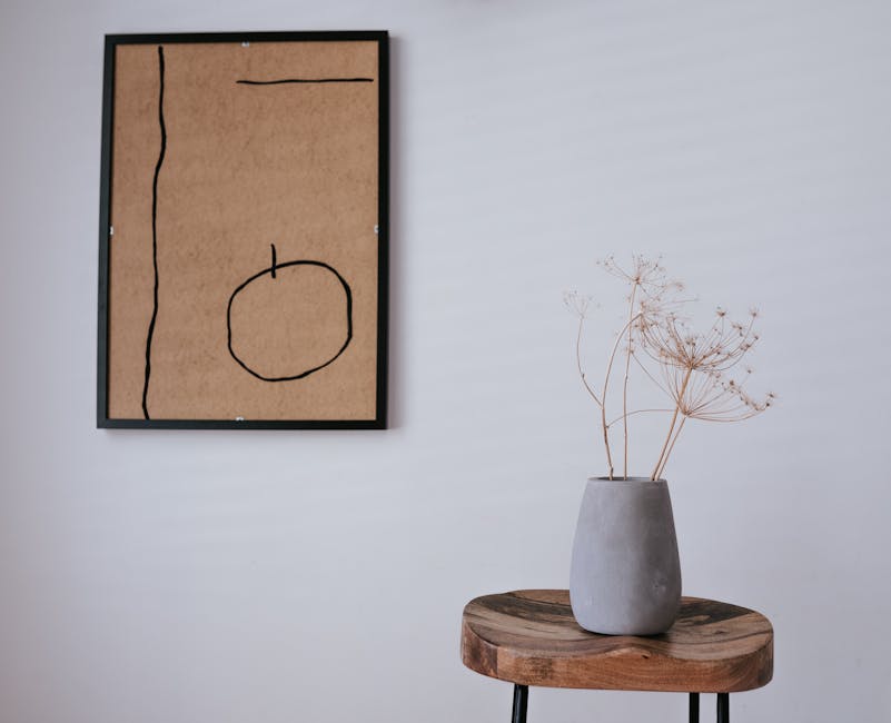 A simple and serene interior with a gray vase on a stool and abstract wall art.