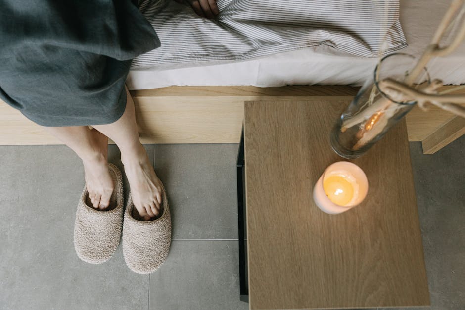 A tranquil bedroom setting featuring slippers, a wooden table, and a lit candle.