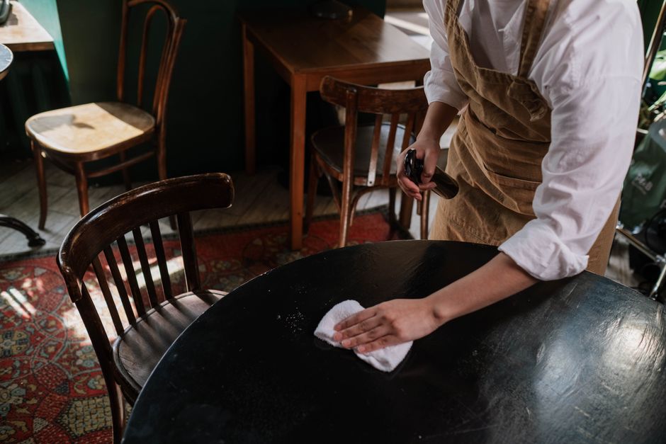 A waitress cleans a table in a cozy café with elegant wooden chairs.