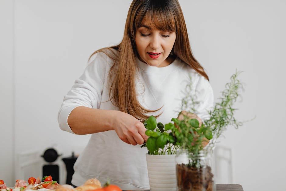A woman in a white sweater tending to a potted herb plant indoors, showing focus and care.