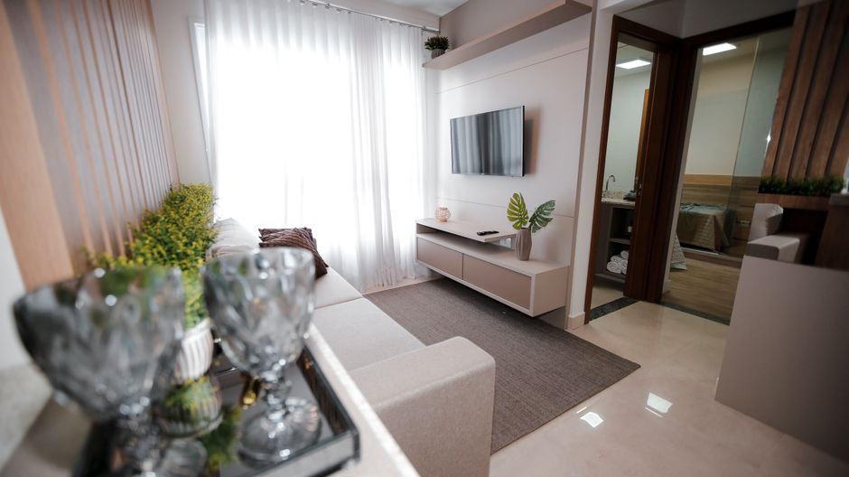 Bright and cozy minimalist living room with light decor and elegant furniture, featuring a wall-mounted TV and lush plants.