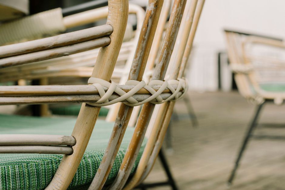 Detailed view of a wickered wooden chair with green cushion in natural light outdoors.