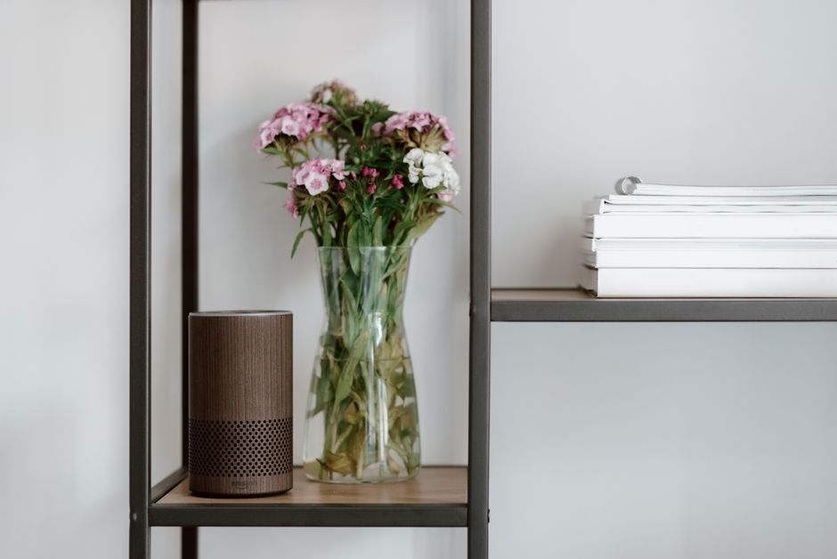 Elegant shelf setup with a smart speaker, vase of flowers, and stacked books for a minimalist touch.