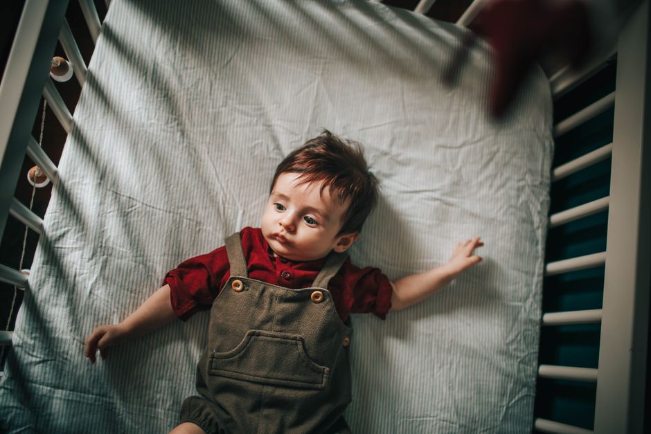 Top view of adorable toddler lying on comfortable mattress in crib and looking away