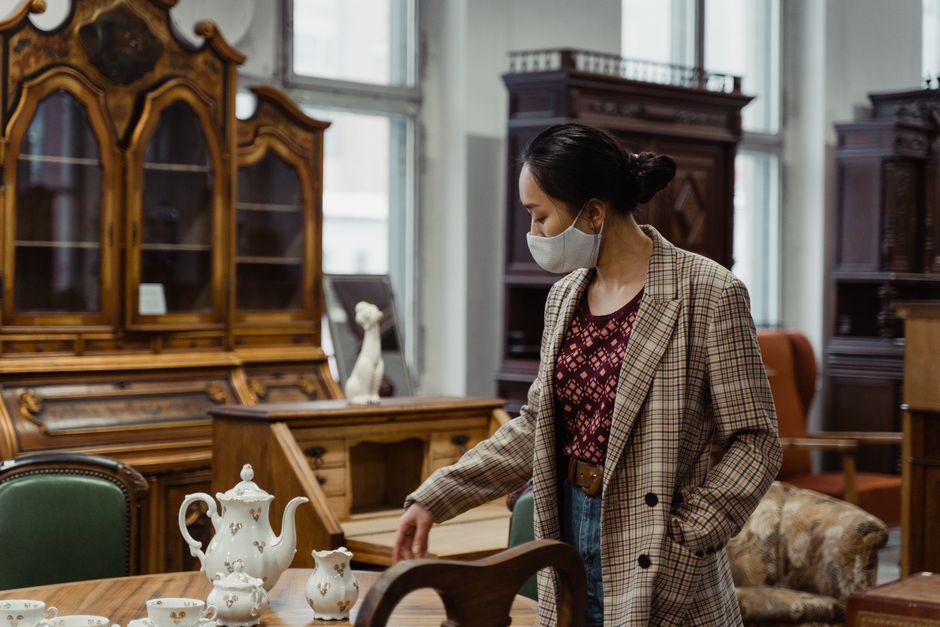 Woman in plaid coat and mask browsing porcelain tea set in antique store.