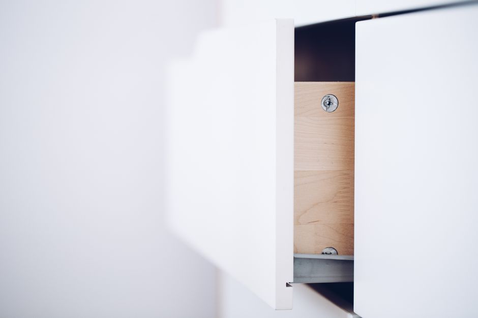 Close-up of an open white drawer revealing a wooden interior and screws in a minimalist design.