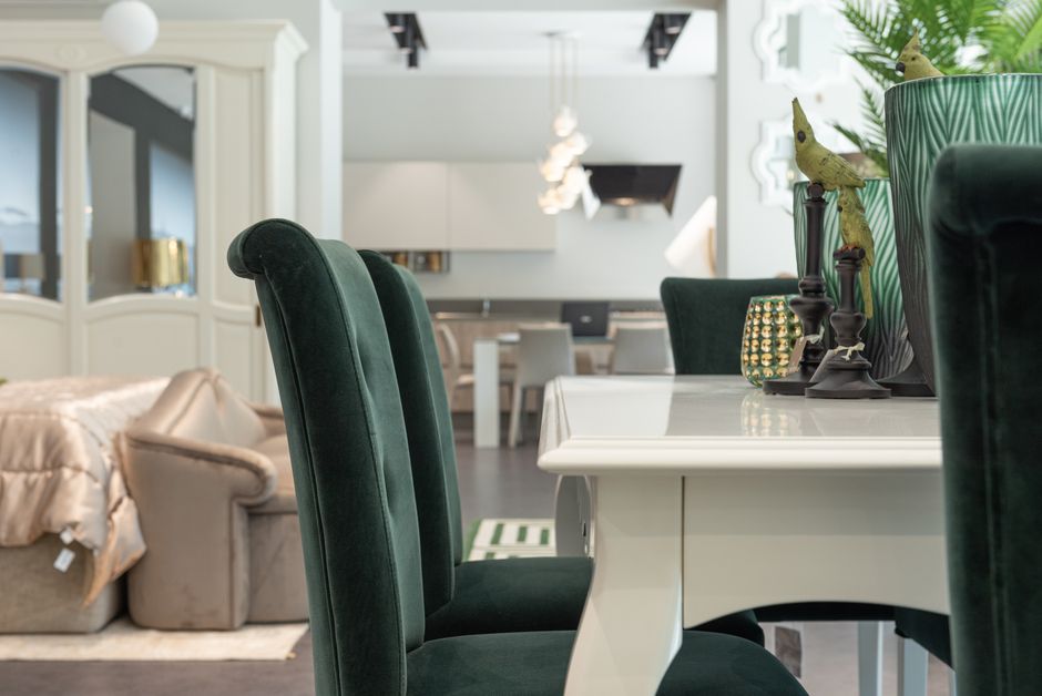 Elegant velour chairs and white table in dining zone of classic styles studio apartment with comfortable bed and kitchen area
