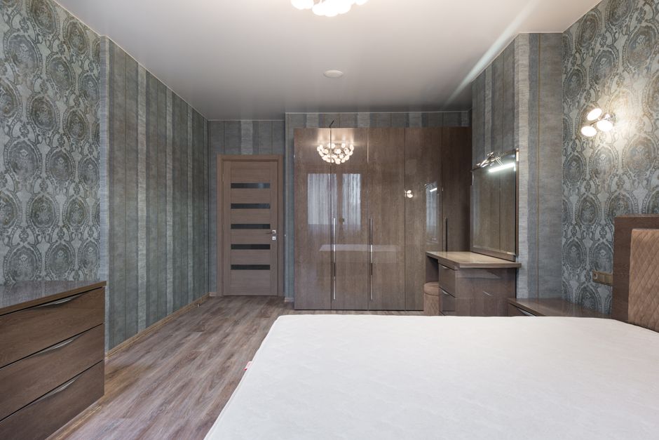 Spacious room with bed and glossy cupboard with wooden dressers under light of chandelier