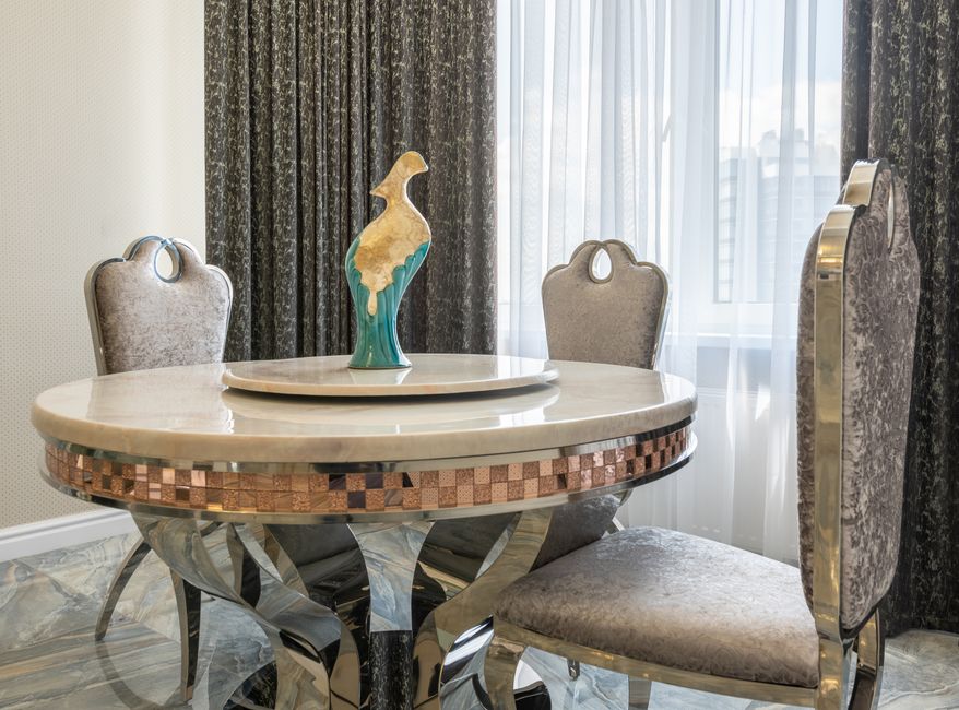 Statuette on round shaped table between classic chairs on marble floor in modern flat with curtains