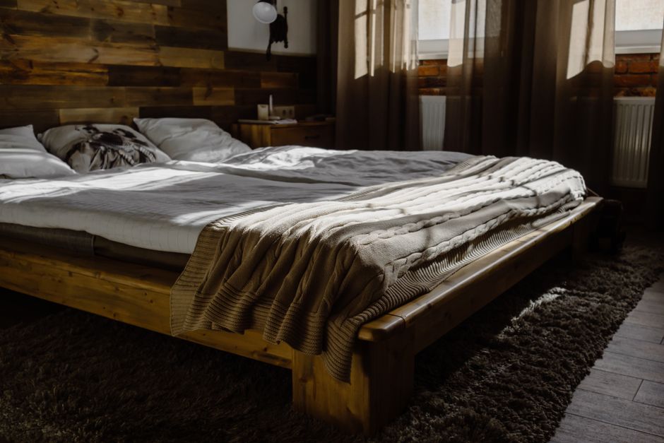 Sunlit modern bedroom with wooden bed frame and cozy blankets, offering interior design inspiration.