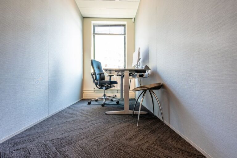 A clean, minimalist office space featuring a desk, chair, and computer by a large window.