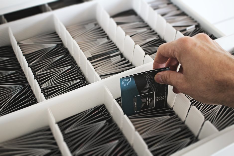 A hand selects a card from an array of organized cards in a white box.