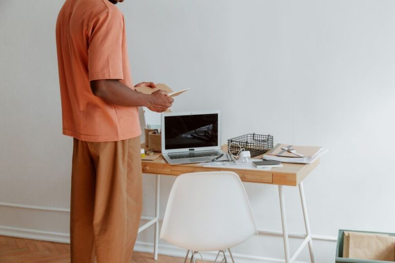 A person standing at a wooden desk with a laptop and office supplies. Minimalist aesthetic.