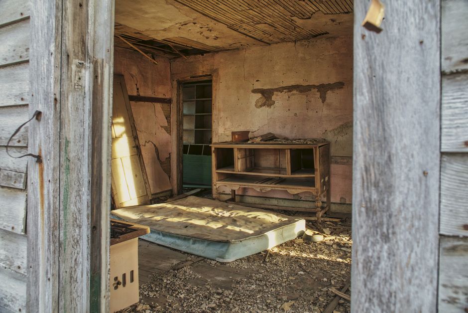 A rustic, abandoned room with a mattress and wooden dresser.