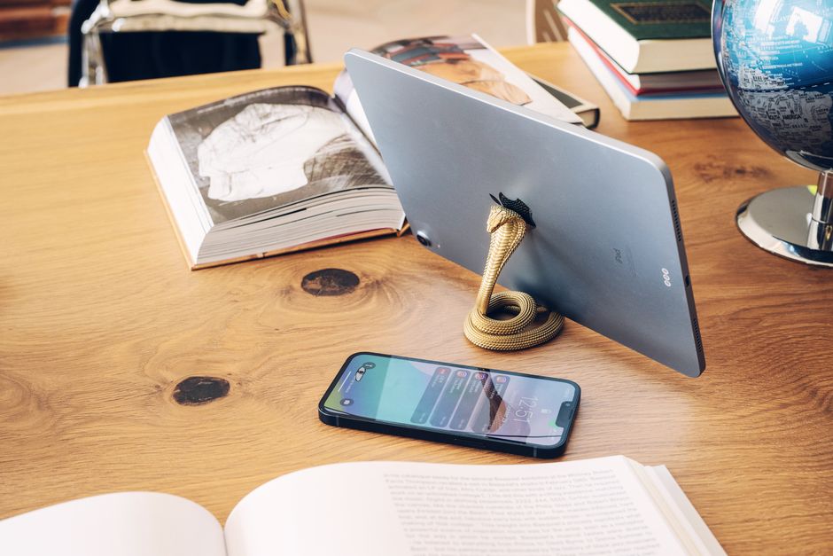 A stylish workspace featuring a tablet with snake holder and books on a wooden desk, ideal for tech setups.