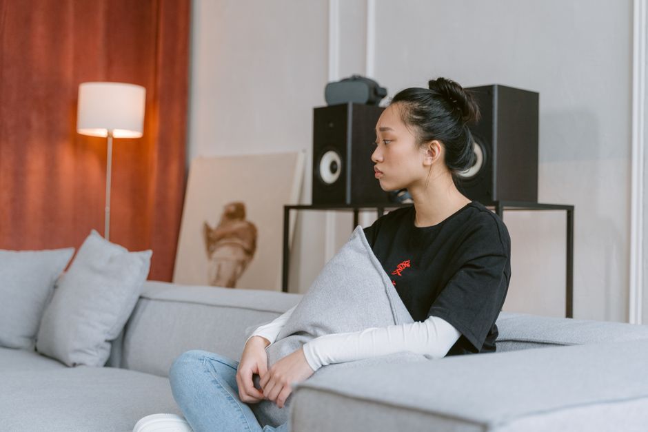 Asian woman sitting thoughtfully on a modern couch with cushions, in a contemporary living room.