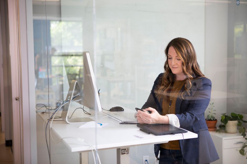 Businesswoman in a blazer using her smartphone at a standing desk in a modern office.