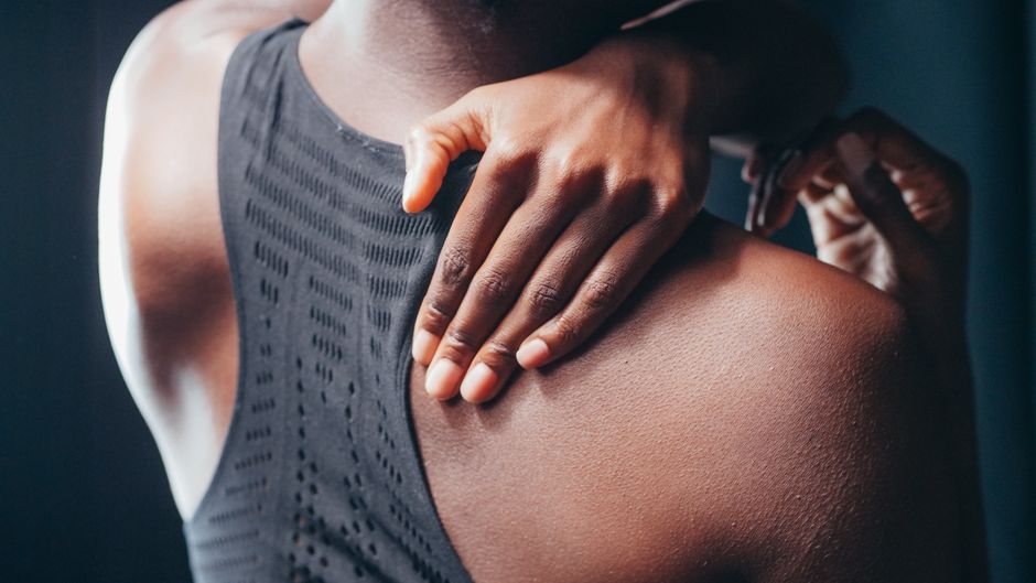 Close-up of a person holding their shoulder, wearing a black sports bra.