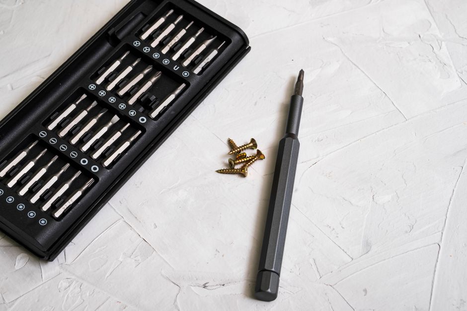 Close-up of a precision screwdriver kit with various bits and screws on a light textured background.