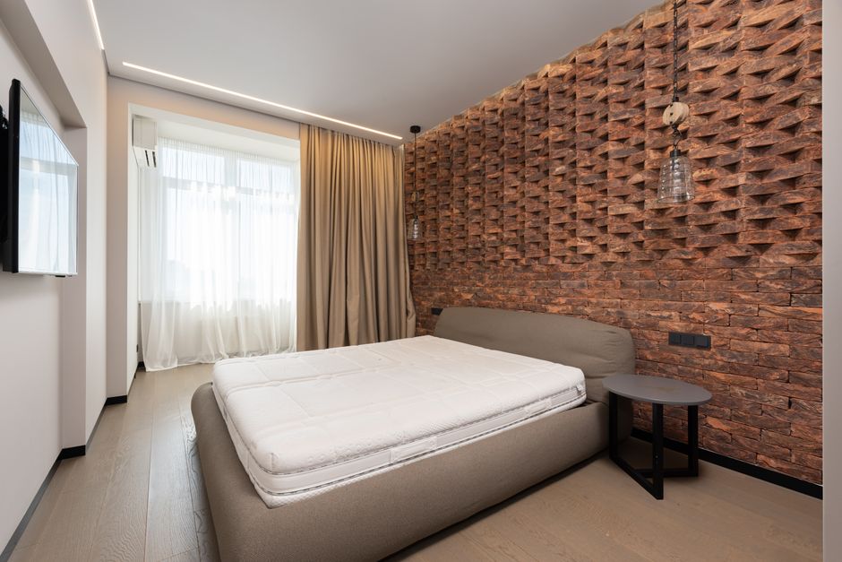 Comfortable bed with mattress placed against modern TV and decorative wall in stylish bedroom with curtains on window at home
