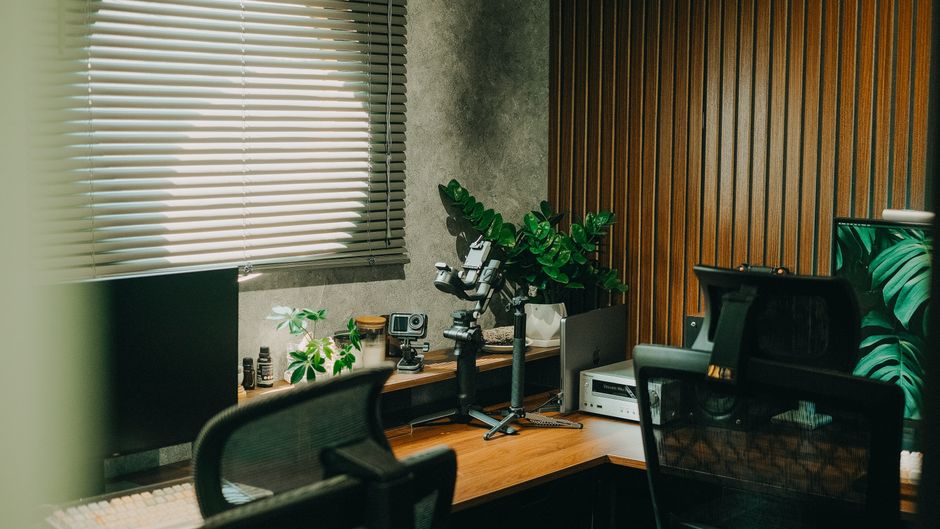 Contemporary home office setup with gadgets, green plants, and natural light through blinds.