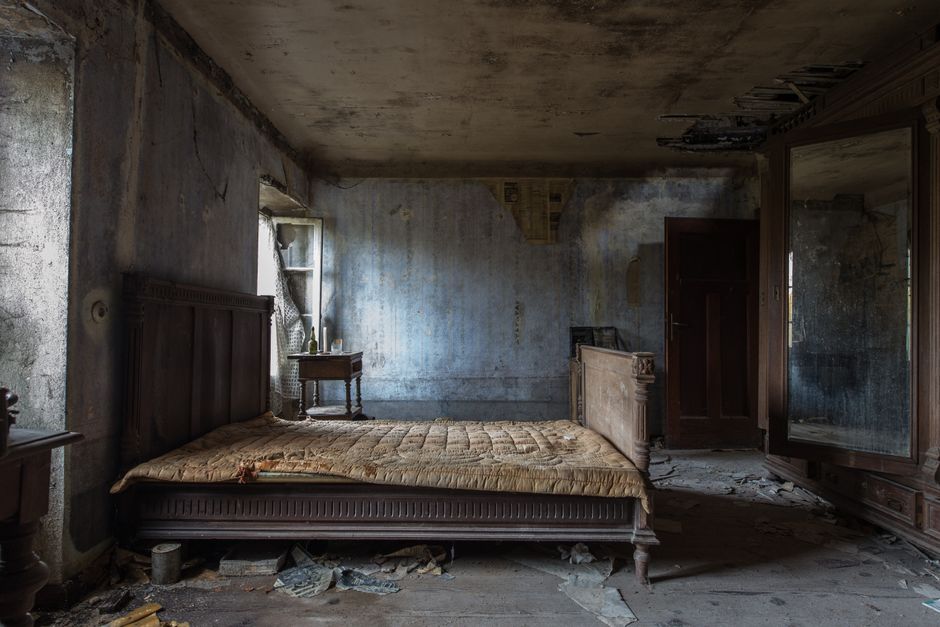 Explore the haunting beauty of an abandoned rustic bedroom, displaying decayed furniture and peeling walls.