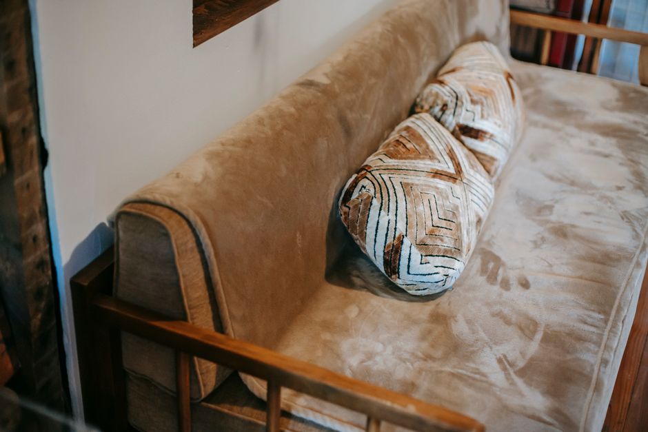 From above of comfortable sofa with plaid and pillows placed in cozy apartment