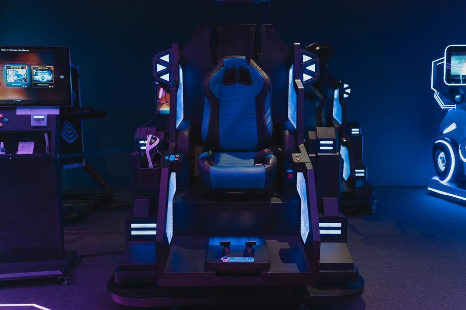 High-tech gaming simulator chair in an indoor arcade setting with neon lights.
