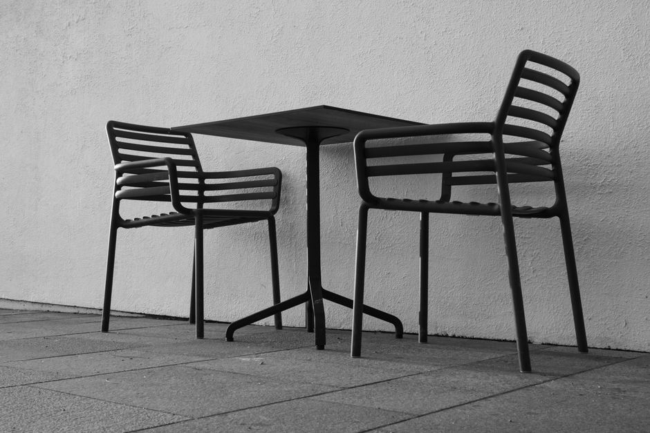 Minimalist black and white photo of an empty outdoor cafe with two chairs and a table.
