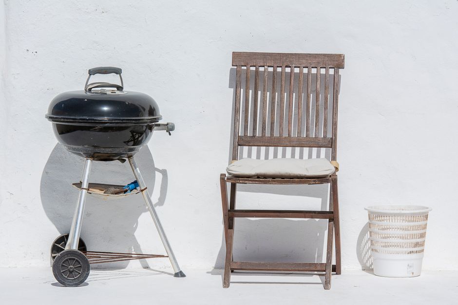 Outdoor scene with a barbeque grill, wooden chair, and white wall, evoking summer relaxation.
