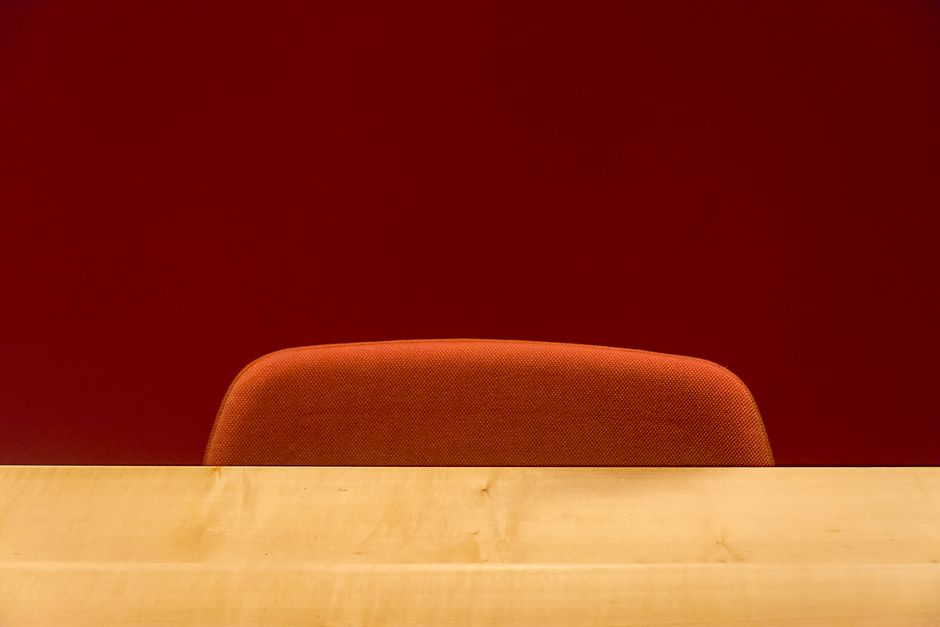 Simple office setup featuring a wooden desk and red chair against a red wall. Ideal for workspace themes.