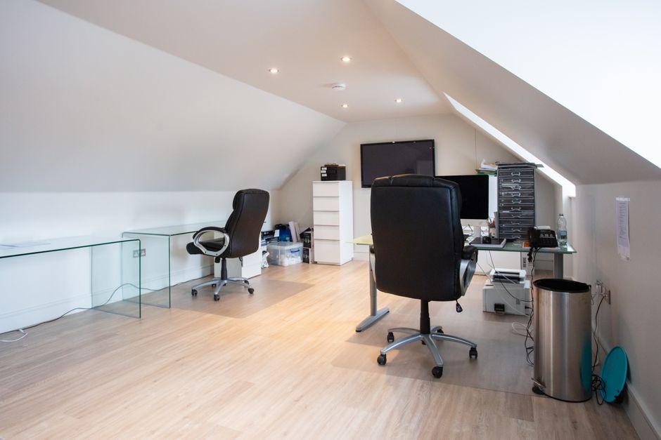 Spacious attic home office with sleek chairs and glass desks, perfect for a productive work environment.