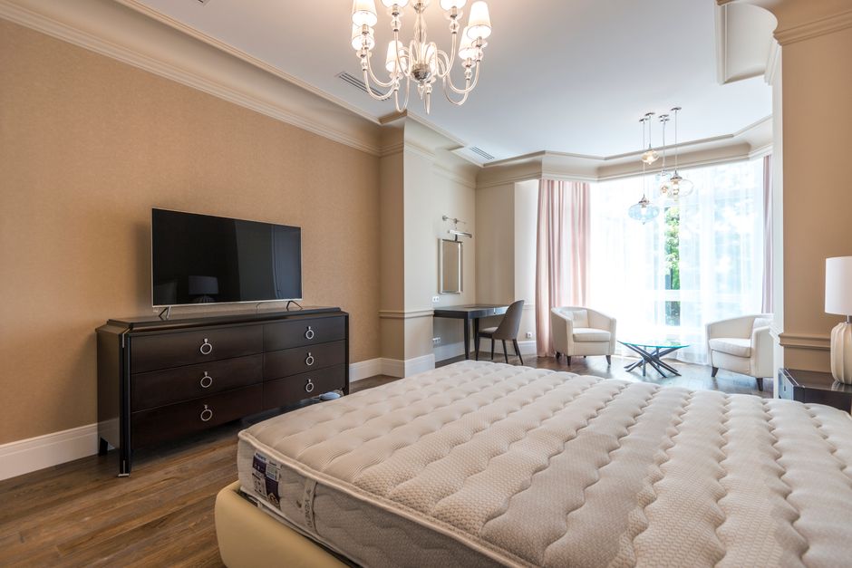 Spacious modern bedroom with chandelier and flat screen TV, featuring a minimalist and elegant design.