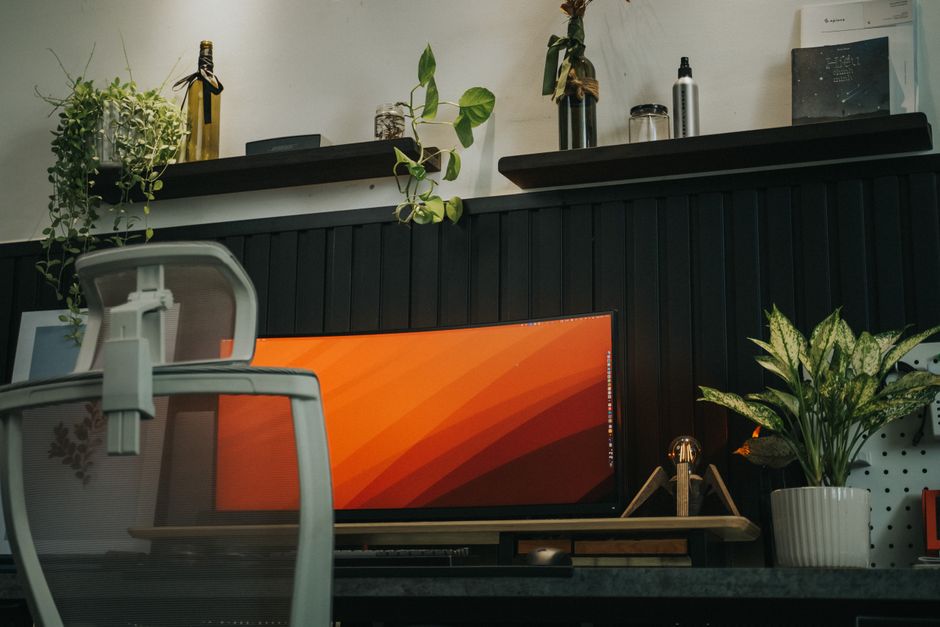 Stylish home office setup featuring a curved monitor, ergonomic chair, and indoor plants for a modern workspace vibe.