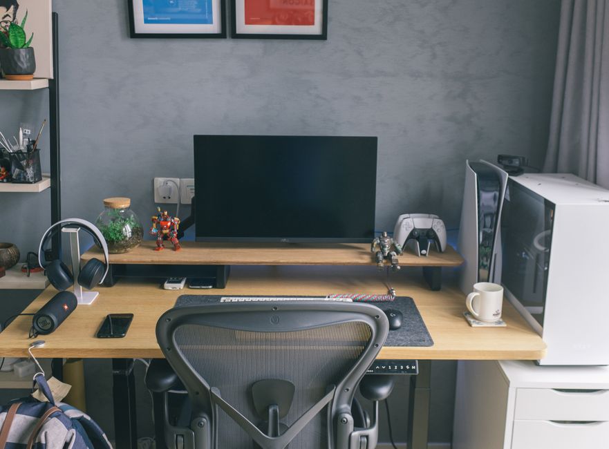 Stylish home office with tech gadgets, computer, and gaming console on a wooden desk.