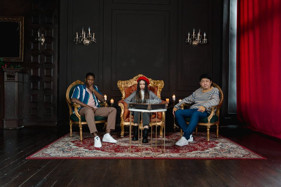 Three individuals in an ornately decorated room with dramatic lighting and furniture.