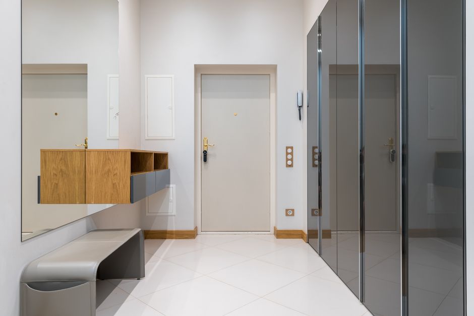 Wooden shelf with bench placed in front of wardrobe with mirrored doors in corridor of modern apartment