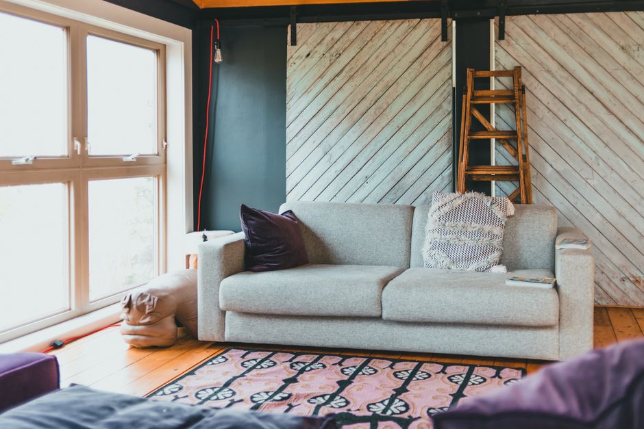 Bright and cozy modern living room featuring a comfortable sofa, wooden ladder, and large windows.