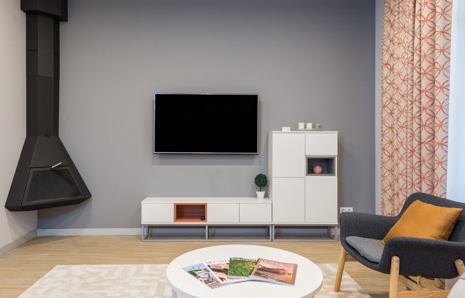 Modern TV and fireplace hanging on wall in minimalist apartment with white furniture and comfortable armchair